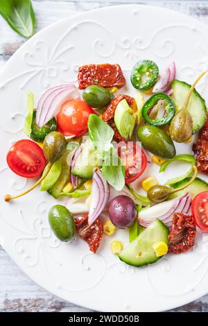 Insalata semplice con olive verdi e calamata, cetrioli, ciliegie e pomodori marinati, Capperi e pepe jalapeno. Sfondo in legno luminoso. Vista dall'alto Foto Stock