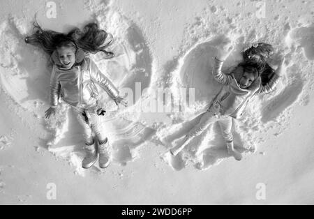 Angeli di neve fatti da bambini nella neve. Bambini sorridenti sdraiati sulla neve con spazio fotocopie. Bambini divertenti che fanno l'angelo della neve. Vista dall'alto. Foto Stock