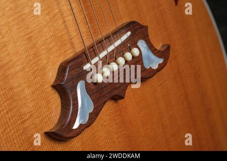 Ponte di chitarra acustica con intarsi in madreperla e corde di chitarra Foto Stock