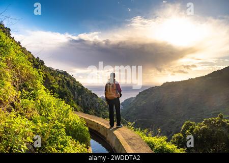 Turista a Levada do Norte sull'isola portoghese di Madeira. Canale di irrigazione di Levada. Escursioni a Madeira. Sentiero stretto vicino alla levada. Verde Foto Stock