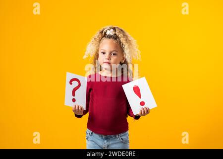 Esplorazione incantevole. Un ritratto di una bambina premurosa che regge carte con punti interrogativi e punti esclamativi, evocando l'essenza di Childr Foto Stock