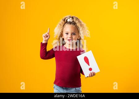 Esplorazione incantevole. Un ritratto di una bambina premurosa che regge carte con punti interrogativi e punti esclamativi, evocando l'essenza di Childr Foto Stock