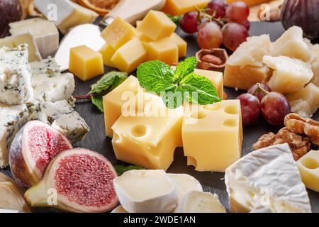 Varietà di formaggi a fette con frutta, menta, noci e taglierini. Un meraviglioso sfondo di formaggi per i vostri progetti. Foto Stock
