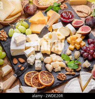Varietà di formaggi a fette con frutta, menta, noci e taglierini. Un meraviglioso sfondo di formaggi per i vostri progetti. Foto Stock