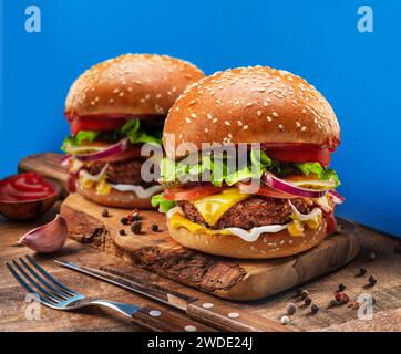 Gustosi cheeseburger o hamburger su vassoio di legno da vicino. Sfondo blu. Foto Stock