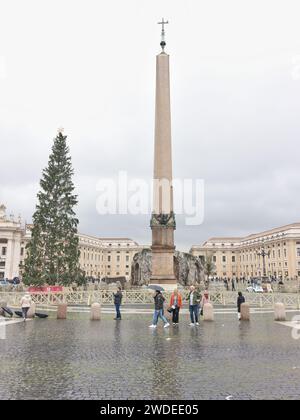 I turisti all'albero di natale accanto all'obelisco nella piazza della basilica di San Pietro, città del Vaticano, Roma, Italia, in un giorno di pioggia. Foto Stock