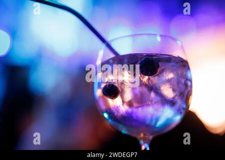 Primo piano di gin e cocktail tonico con mirtilli, illuminato da incantevoli luci multicolori sullo sfondo. Foto Stock