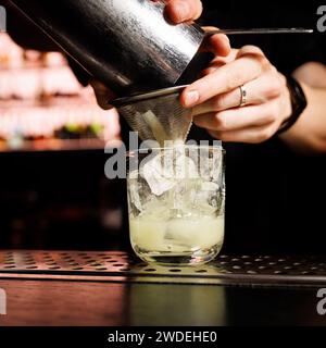 Il barista versa un cocktail misto in un bicchiere con ghiaccio. Foto Stock
