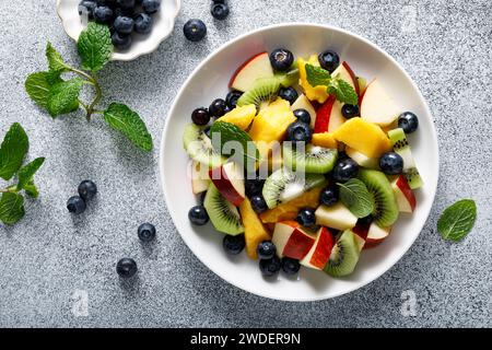 Insalata di frutta e frutti di bosco con mango, kiwi, mela, mirtilli e foglie di menta fresca. Cibo sano, dieta. Vista dall'alto Foto Stock