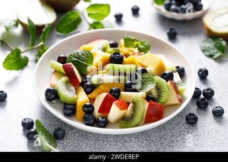Insalata di frutta e frutti di bosco con mango, kiwi, mela, mirtilli e foglie di menta fresca. Cibo sano, dieta Foto Stock