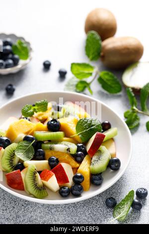 Insalata di frutta e frutti di bosco con mango, kiwi, mela, mirtilli e foglie di menta fresca. Cibo sano, dieta Foto Stock