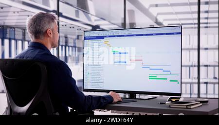 Uomo d'affari che lavora su Gantt Chart utilizzando il computer su Office Desk Foto Stock