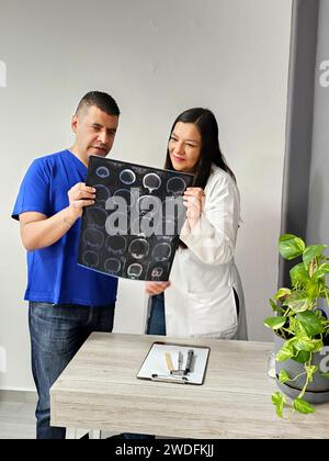 Neurologo latina medico specialista donna e infermiere maschile dalla pelle scura esaminano la radiografia del cervello del paziente per discutere di casi di studio e ricerche straordinari Foto Stock