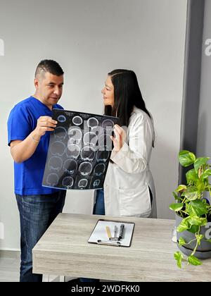 Neurologo latina medico specialista donna e infermiere maschile dalla pelle scura esaminano la radiografia del cervello del paziente per discutere di casi di studio e ricerche straordinari Foto Stock