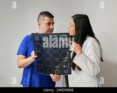 Neurologo latina medico specialista donna e infermiere maschile dalla pelle scura esaminano la radiografia del cervello del paziente per discutere di casi di studio e ricerche straordinari Foto Stock