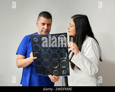 Neurologo latina medico specialista donna e infermiere maschile dalla pelle scura esaminano la radiografia del cervello del paziente per discutere di casi di studio e ricerche straordinari Foto Stock