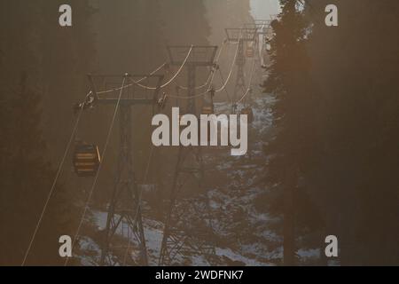 Srinagar Kashmir, India. 20 gennaio 2024. I turisti siedono in una funivia mentre passa sopra il tratto più alto di Affarwat, a Gulmarg, a circa 55 km da Srinagar. Il prolungato periodo di secchezza di quest'inverno nella valle del Kashmir ha inferto un duro colpo alla famosa stazione sciistica di Gulmarg. Le piste da sci, un tempo trafficate, sono ormai senza neve e sono motivo di delusione per i turisti e in particolare per gli appassionati di sci. L'assenza di nevicate stagionali ha comportato la cancellazione delle prenotazioni di massa per i proprietari di hotel, con un grave impatto sulle loro attività. Questa battuta d'arresto imprevista sottolinea la vulnerabilità Foto Stock