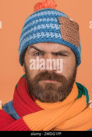 Abbigliamento autunno-inverno. Ritratto di primo piano uomo serio attraente con barba e baffi in cappello e sciarpa lavorati a maglia colorata. Moda autunno-inverno maschile Foto Stock