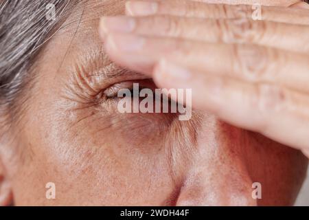 Primo piano di una donna matura che strizza l'occhio con la mano sulla fronte Foto Stock