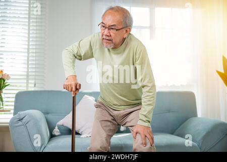 Asian Old Man con occhiali che battono per alzarsi dal divano con bastone da passeggio Foto Stock