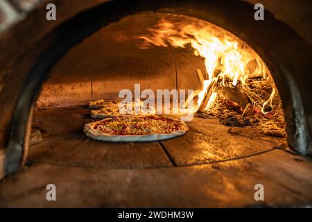 Forno tradizionale per cuocere la pizza con legno bruciato e pala. Diverse pizze sono cotte in un forno a mattoni. Foto Stock