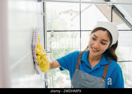 La cameriera che indossa guanti protettivi pulisce le piastrelle di ceramica con un panno in microfibra nel bagno Foto Stock