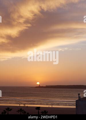 Cieli spettacolari al tramonto sul mare e sull'isola mentre la gente cammina sulla spiaggia di Essaouira, Marocco, 20 gennaio 2024 Foto Stock