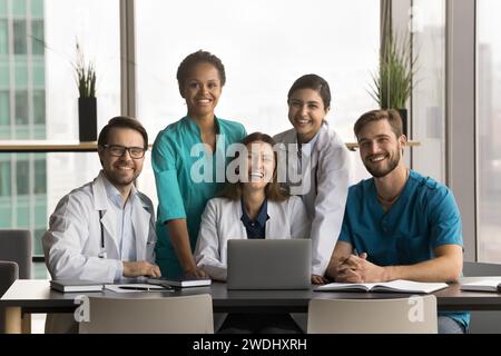 Team eterogeneo di giovani medici felici seduti al computer portatile Foto Stock