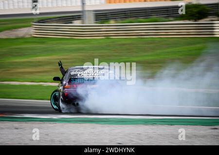 Auto ad alta velocità alla deriva con il fumo e infilando un braccio fuori dal finestrino intorno al circuito Ricardo Tormo a Cheste, Valencia, Spagna Foto Stock