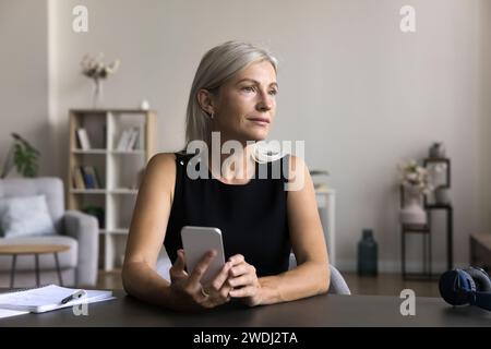 Donna premurosa che utilizza uno smartphone moderno sul luogo di lavoro Foto Stock