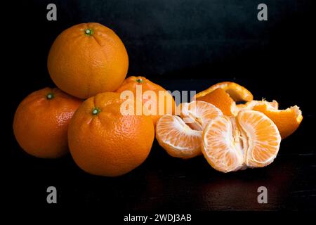 Una pila di quattro tangerini su sfondo scuro. Frutti d'arancia su sfondo nero. Agrumi in cucina. Una pila di quattro tangerini su una schiena scura Foto Stock