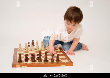 Bambino che gioca a scacchi, sfondo bianco studio. Un bambino con pezzi di scacchi su una scacchiera Foto Stock