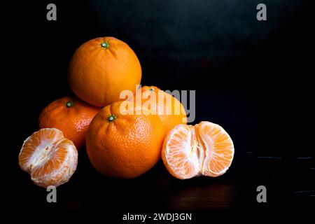 Una pila di quattro tangerini su sfondo scuro. Frutti d'arancia su sfondo nero. Agrumi in cucina. Una pila di quattro tangerini su una schiena scura Foto Stock