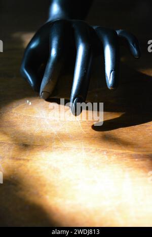 Statuetta nera di una mano femminile opaca su un legno marrone con un raggio solare. Foto Stock