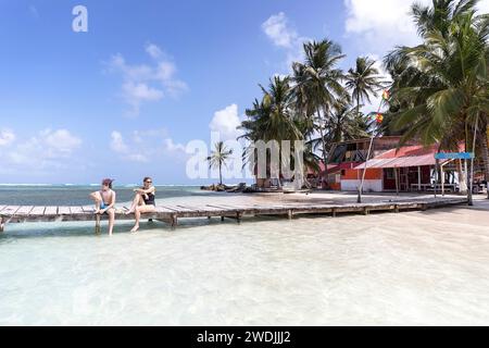 Madre e figlio, turisti, seduti su un molo di legno su una spiaggia sabbiosa, godendosi le vacanze su un'isola tropicale, sull'arcipelago di San Blas, Panama Foto Stock