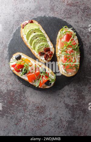 Panini aperti freschi con rucola, jamon, pomodori secchi, avocado, formaggio spalmabile, primi piani di olive e peperoni arrostiti su un tabl di ardesia Foto Stock