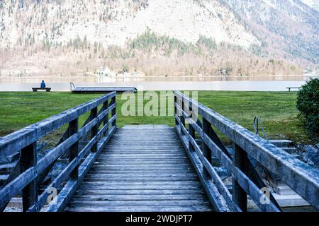 Un ponte di legno in un campo verde che si affaccia su un lago tra le montagne Foto Stock