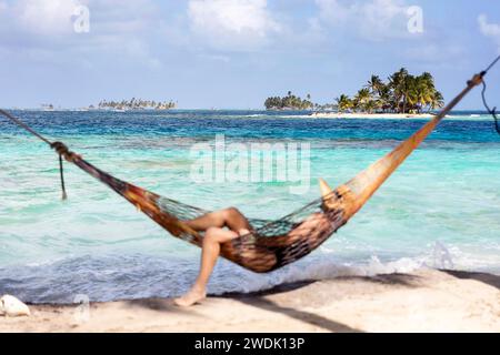 Donna turistica in un'amaca con cappello di paglia sulla testa che si rilassa su un'idilliaca isola tropicale nel territorio indigeno di Guna Yala a Panama Foto Stock