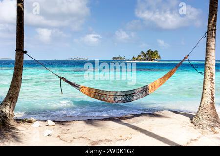 Un'amaca tra palme su un'idilliaca isola tropicale nel territorio indigeno di Guna Yala a Panama, con spettacolari isole tropicali sul retro Foto Stock