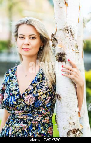 Ritratto ravvicinato all'aperto di una donna bionda appoggiata su un albero Foto Stock