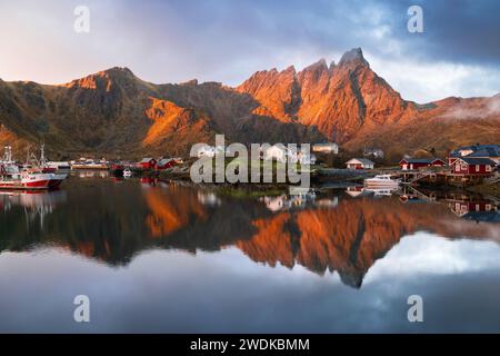 Riflessi di case e montagne nell'acqua del villaggio di Ballstad durante l'alba, Vestvagoy, Nordland, Isole Lofoten, Norvegia, nord Europa Foto Stock