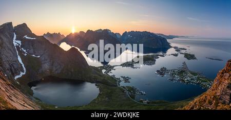 L'ampio panorama da Reinebringen mostra il sole di mezzanotte sulle isole Lofoten, Norvegia, illuminando il villaggio di Reine con i suoi fiordi Foto Stock