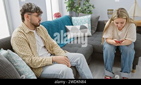 Una donna che usa uno smartphone e un uomo seduto insieme su un divano in un soggiorno moderno. Foto Stock