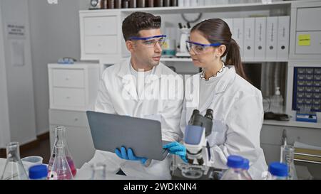 Uomini e donne scienziati in camici da laboratorio discutono di ricerche usando una tavoletta in un ambiente di laboratorio Foto Stock