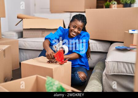 Donna afroamericana sorridente sicuro imballaggio scatola di cartone in nuova casa Foto Stock