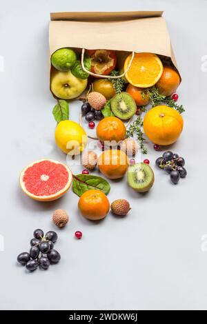 Frutta in sacchetto di carta. Cachi, kiwi e arancia sul tavolo. Sfondo grigio. Spianatura piatta Foto Stock