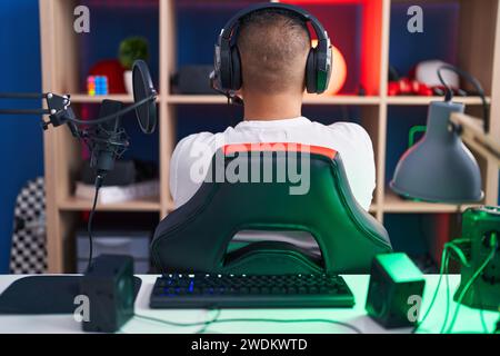 Giovane ispanico che gioca ai videogiochi in piedi indietro guardando lontano con le braccia incrociate Foto Stock