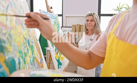 Due artisti, un uomo e una donna, che approfondiscono profondamente la loro arte! riuniti in uno studio accogliente, la creatività senza ostacoli si sviluppa su tela. Foto Stock