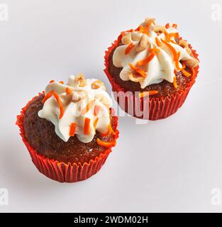 Due cupcake di carote smerigliate con fodere rosse su sfondo bianco, allettanti e pronti da mangiare. Foto Stock