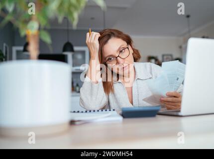 Bella donna pensiva di mezza età in occhiali con bollette mensili che pensano al budget familiare. Piccole imprese, finanze domestiche, risparmio di denaro conc Foto Stock